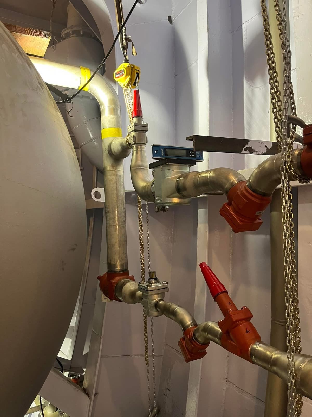 Pipe fittings with red valve handles beside a tank